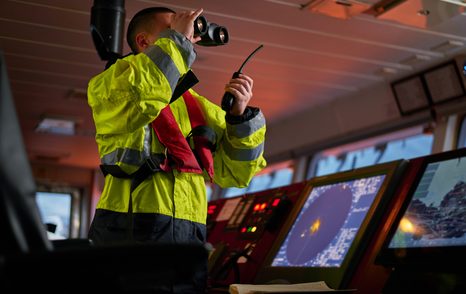 navigator wearing life jacket using binoculars and using vhf radio