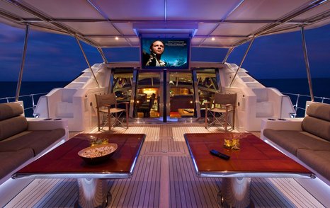 Two tables undercover on yacht deck with large TV screen visible above glass doors.