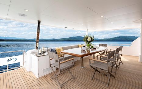 Al fresco dining area onboard Horizon FD80, dining table and eight chairs overlooking sea and mountain range in background.