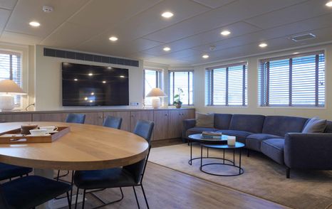 Main salon onboard superyacht Better Space. Oval dining table in foreground with sofa and extensive glazing aft.