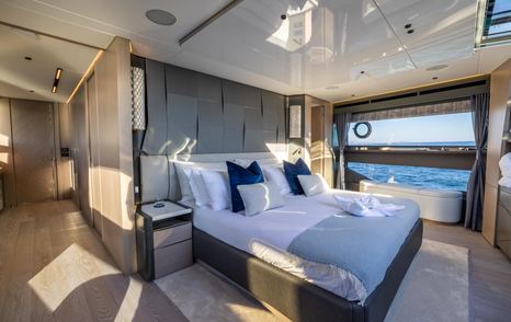 Master cabin onboard Sunseeker 100 Yacht, central berth facing starboard, with walkway in foreground and large window in background looking out over sea.