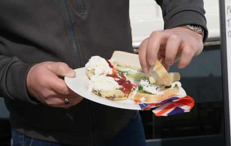 James Barke holding a messy plate of cucumber sandwiches and scones with cream and jam during the £300,000 used boat challenge.
