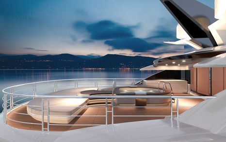 Sundeck of Rossinavi Florentia superyacht with light colored furniture and teak deck. Sea in foreground with hills light up by specks of house lights