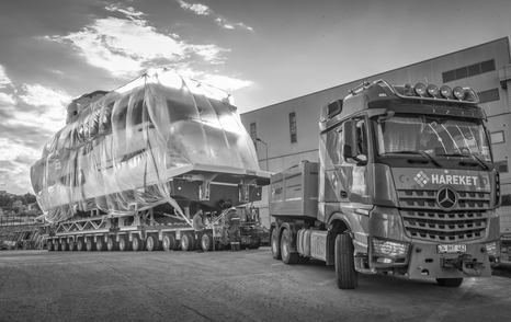 Black and white image of Numarine 26XP being pulled on a trailer alongside shipyard construction building