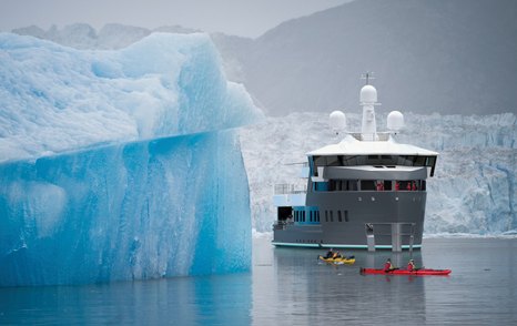 Frontal image Damen SeaXplorer 55 underway next to an iceberg, surrounded by arctic environment and canoes in the foreground