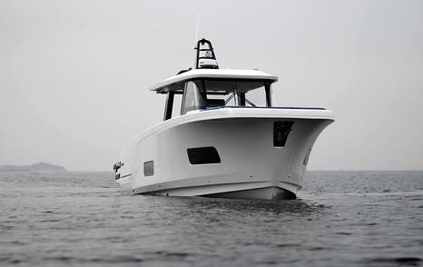 Front three-quarter view of the AIATA Sunfinder 50 running at sea, showing the upright bow, enclosed wheelhouse and clean white hull lines.
