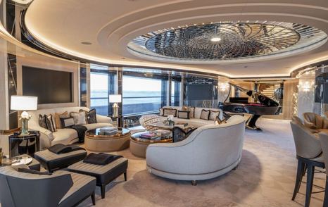 Overview of interiors onboard motor yacht KISMET, with plush cream seating and a grand piano in the background