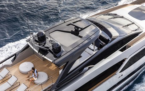 sundeck on board Argo 90 with man sitting down, sun pads, and glass hard top covering a seating area