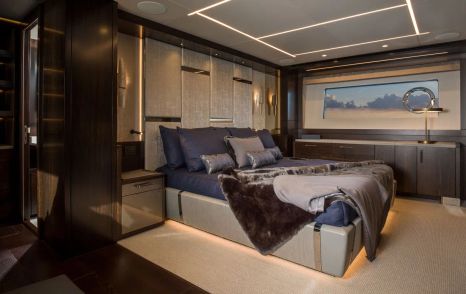 Overview of Sunseeker 88 Yacht master cabin, central berth with wide window in background, fitted out in natural brown tones.