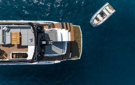 Aerial view looking down on Sunseeker 75 Sport Yacht, aft main deck visible with tender sat adjacent to yacht in the water.