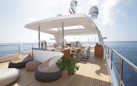 Overview of a sun deck onboard a Benetti motor yacht, with bean bag seating in the foreground and alfresco dining aft