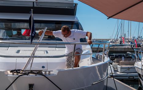 A man is peering down over the rail at the bow of a yacht which is berthed at the Cannes Yachting Festival