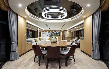 Rear view of Horizon Yachts FD102 interior dining area, large oval dining table surrounded by white upholstered chairs and curtains 