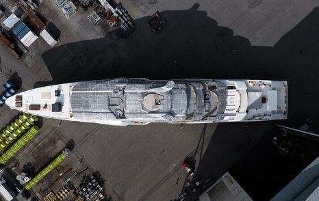 Aerial view looking down on Oceanco Project Y722 on tarmac outside construction shed.