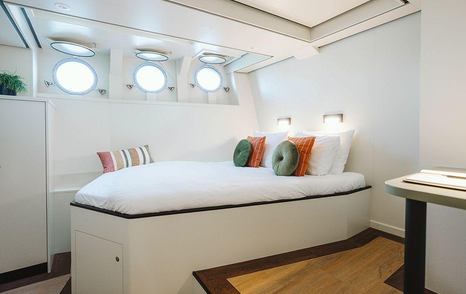 Guest cabin on motor yacht Scintilla Maris with double bed, orange and green furnishings and white bedding