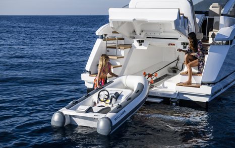 one lady sits on the steps and one lady helps pull a tender into its storage facility on the aft deck of the Targa 45