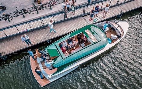 Limousine tender viewed from above at harbour with people on board and people on decking next to tender