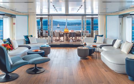 Upper salon onboard CRN RIO superyacht. Sofas sat facing against opposite walls with al fresco dining area visible in background.