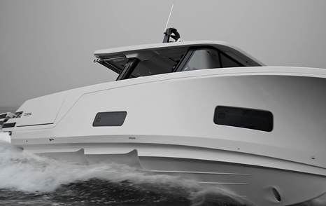 Close side view of the AIATA Sunfinder 50 hull with dark hull windows and pronounced spray rails cutting through light chop.