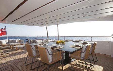 Aft deck onboard motor yacht LOUI with an alfresco dining table surrounded by padded seats