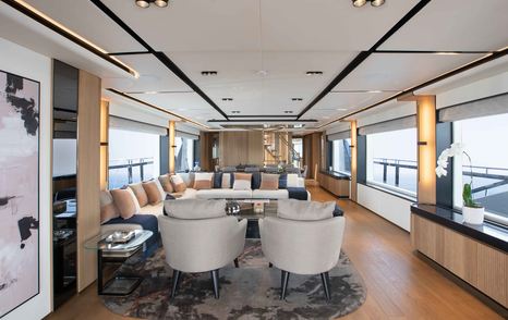 Overview of the main salon onboard the Majesty 111, L shape sofa in background with armchairs forward, surrounded by wide stretches of glazing.