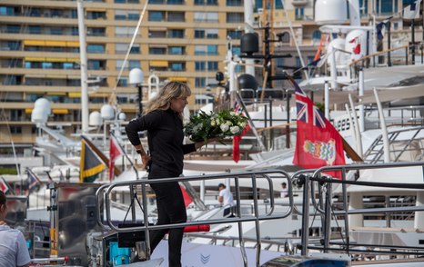 Female dressed in black standing on the bow of a superyacht at the Monaco Yacht Show, Monte Carlo visible in background.