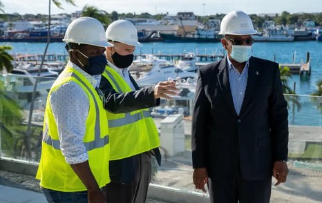 Bahamas Prime Minister Dr. Hubert Minnis tours Hurricane Hole Superyacht Marina at Paradise Landing, with two construction representatives. Moored superyachts in background.