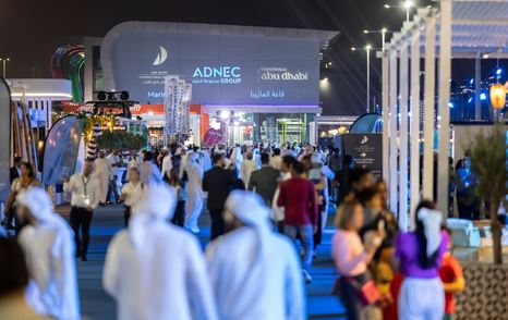 Visitors to the ADIBS strolling along exhibitors at night with ADNEC in the background