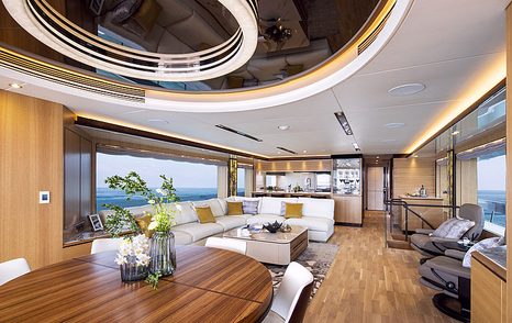 Long view of Horizon Yachts FD102 main salon, large oval dining table and chairs adjacent to L shaped seating, surrounded by wide windows