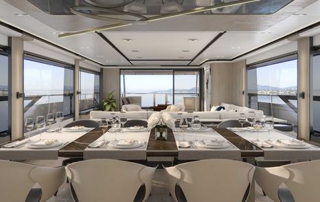 Overview of interior dining area onboard Majesty 111. Long table with white chairs horizantal in foreground with lounge area visible behind.