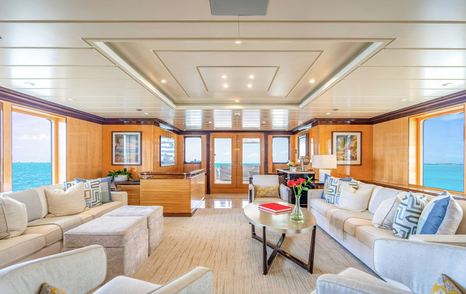 Motor yacht Nita K II's main saloon with cream sofas, patterned cushions, central coffee table, and large windows offering ocean views on both sides