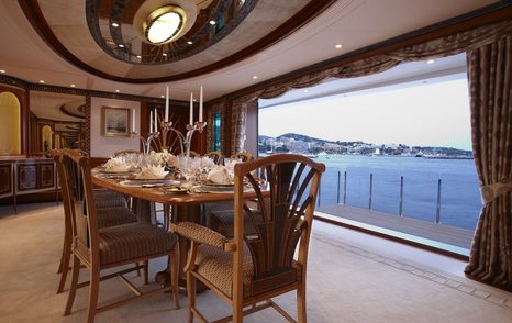 Formal dining room aboard Lady Christine with polished wood table, candelabra centerpiece, and fold-down terrace doors opening to sea views.