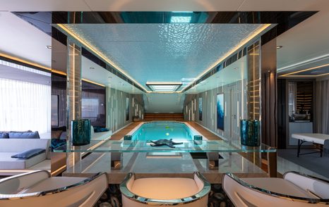 Beach club onboard superyacht TATIANA, indoor pool center with seating in foreground and closed transom door in background. 