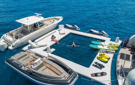 Motor yacht Nita K II's floating yacht beach club setup with inflatables, tenders, jet skis, paddleboards, and people swimming in clear blue water.