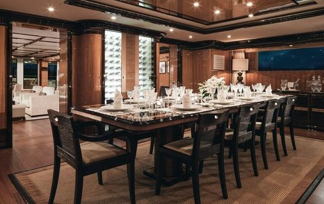 Formal dining area onboard M/Y MEAMINA, long table surrounded by seats in a dark dining set up.