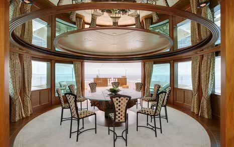 Lady Christine’s observation lounge with circular dining table, wood finishes, high-back chairs, and wraparound windows offering panoramic sea views.