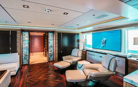 Motor yacht W's main saloon with reclining leather chairs, large flat-screen TV, wooden floors, and windows showing ocean views.