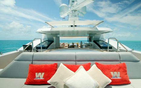 Yacht sun deck with cushioned seating, red and white pillows, and ocean view under clear blue sky