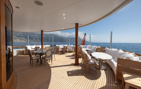 Curved aft deck of superyacht Wedge Too with outdoor dining tables, lounge seating, and sea views