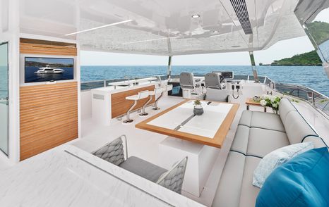 Open flybridge onboard Horizon FD75, central table surrounded by L shaped seating adjacent to TV screen with helm station in background.