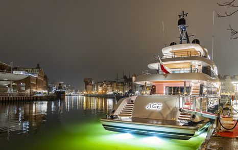 ACE C144S shown at night time in busy harbor with yachts in background, yacht has night lights illuminating the water