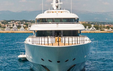 Frontal view of the bow on megayacht IJE, surrounded by sea and superyachts berthed in a marina in the background.