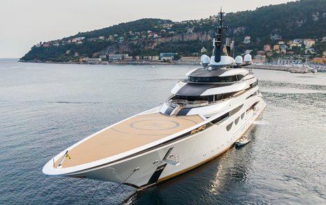 Frontal view of helipad on bow of megayacht AHPO, elevated terrain and buildings visible in far background.