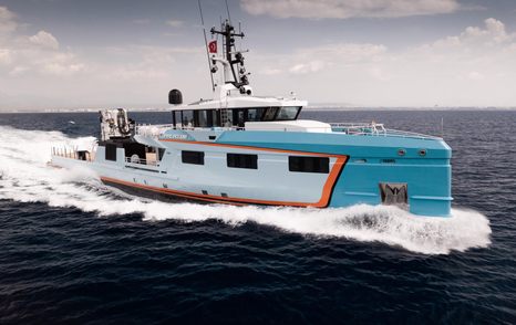 Five Oceans 53m yacht by Damen shown from starboard bow, along side profile in a mid aerial view running shot, making wake in smooth sea with cloudy sky in background