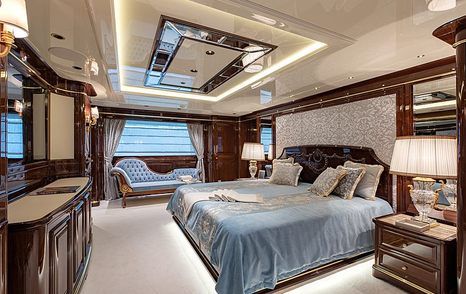 Master cabin onboard Sanlorenzo Lady Lena, central berth facing large mirror on wall, chaise longue against far window and bedside table with lamp