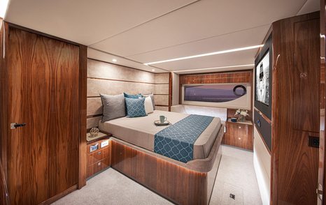 Master cabin onboard Riviera 645 SUV, central berth facing widescreen TV on wall and window on far side.