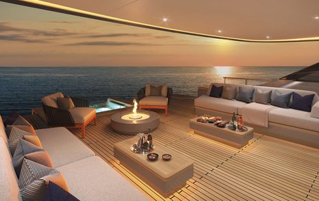 Overview of the aft main deck onboard Benetti superyacht OPUS at sunset, plush seating around the edges facing towards a table with the sunset in the background over the sea.