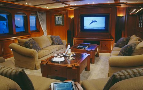 Lounge area onboard sailing yacht ATHENA. Flatscreen TV on wall with sofas arranged around two coffee tables.