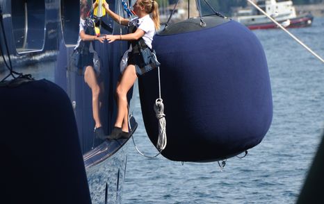 giant fender in background of female crew in harness washing yacht