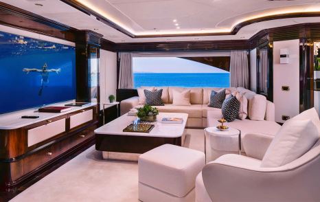 Superyacht Dilara's upper lounge with curved white seating and mounted TV